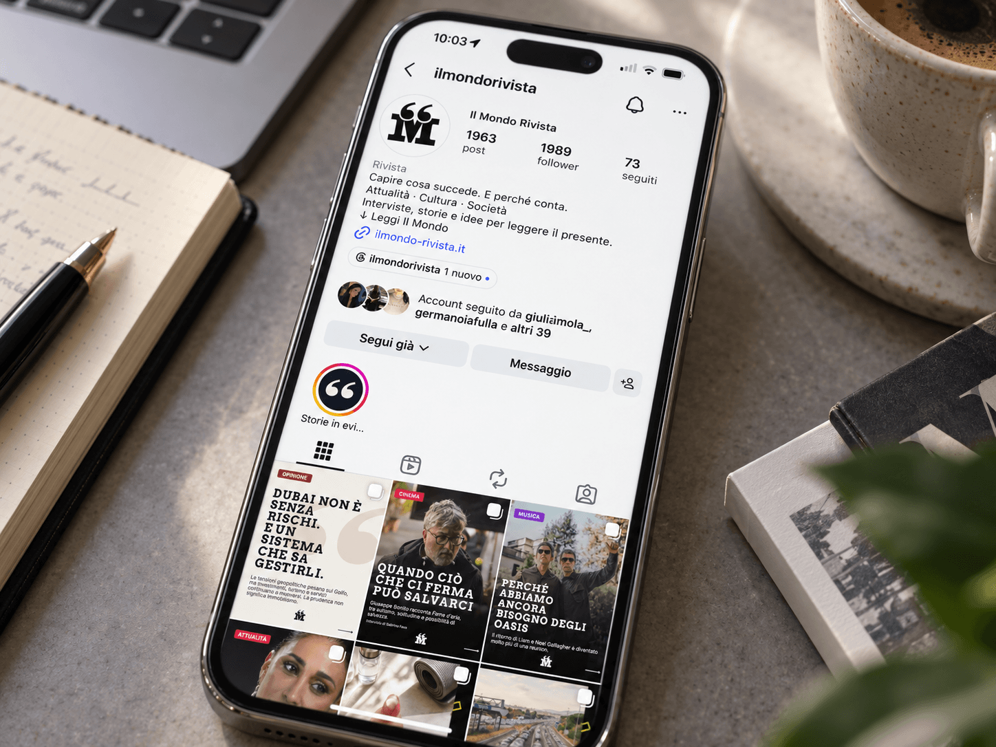 iPhone con il profilo Instagram Il Mondo Rivista su una scrivania con taccuino e caffè.