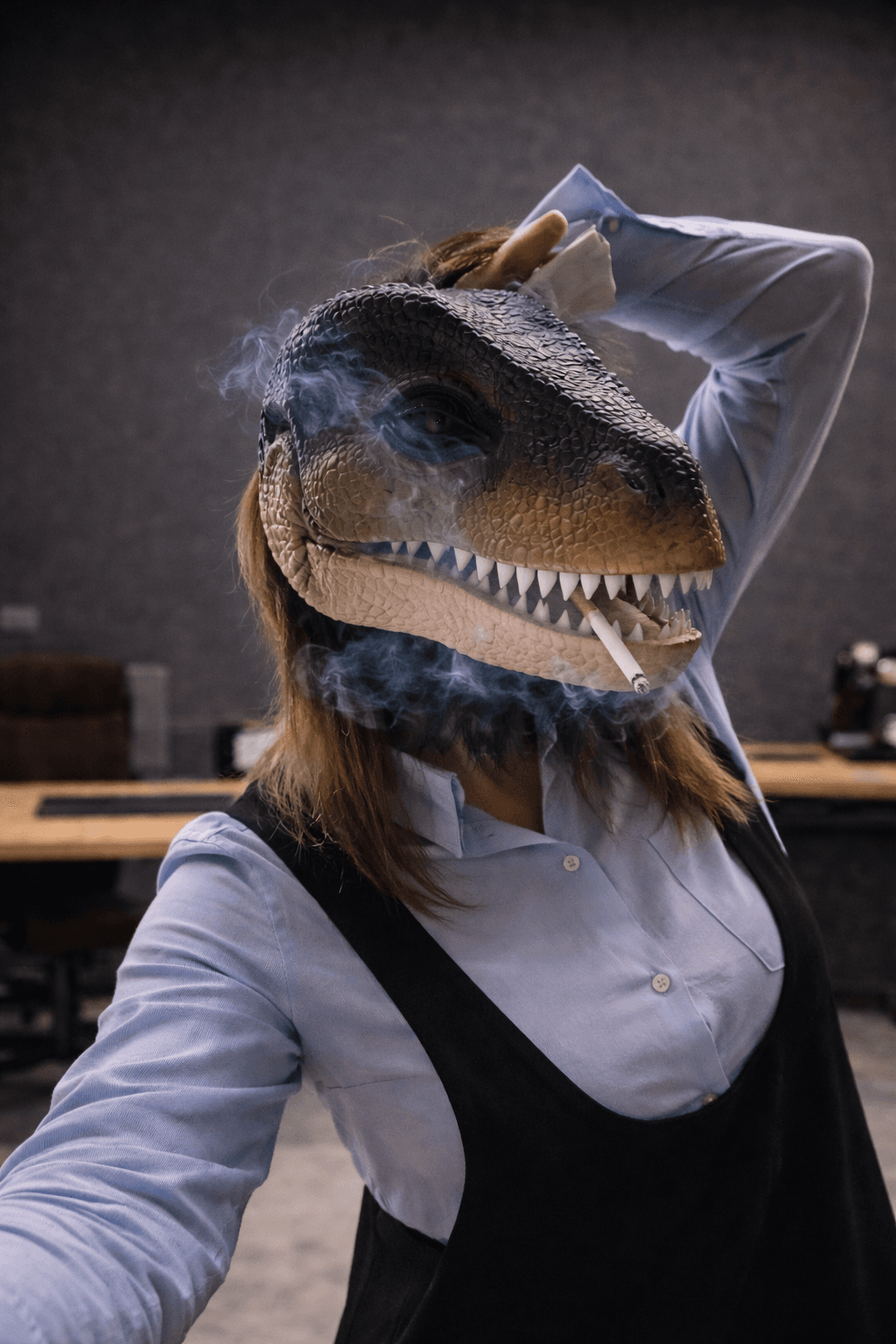 Persona con maschera realistica da dinosauro che fuma una sigaretta in un ufficio con fumo.