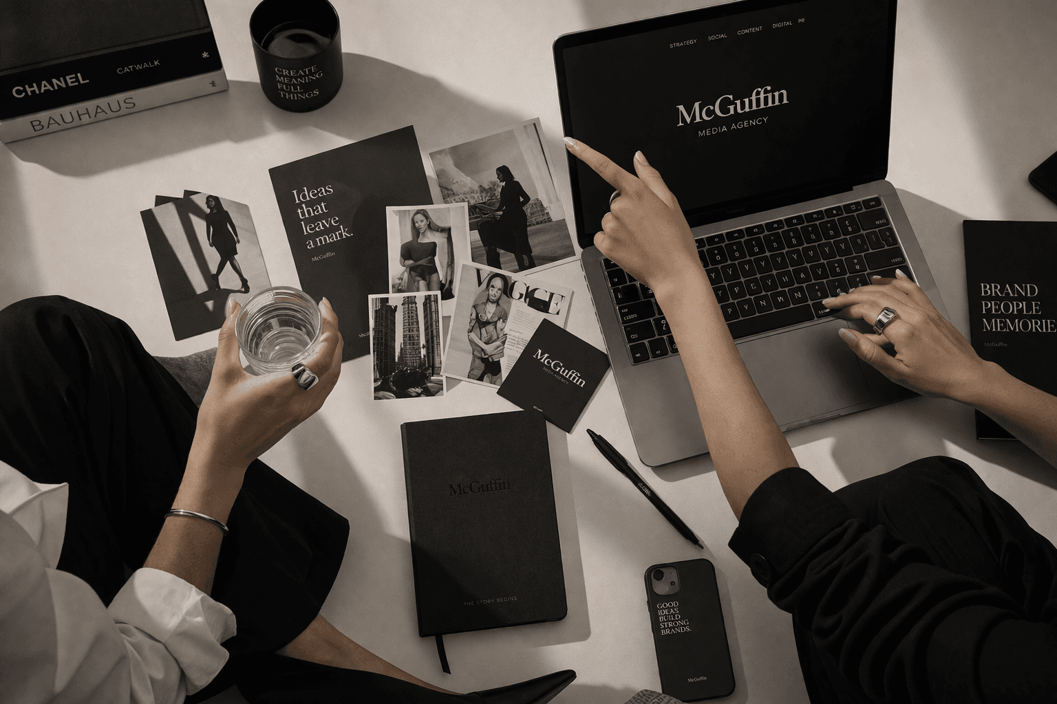 Due persone collaborano su una scrivania con laptop, fotografie e materiale di branding McGuffin.