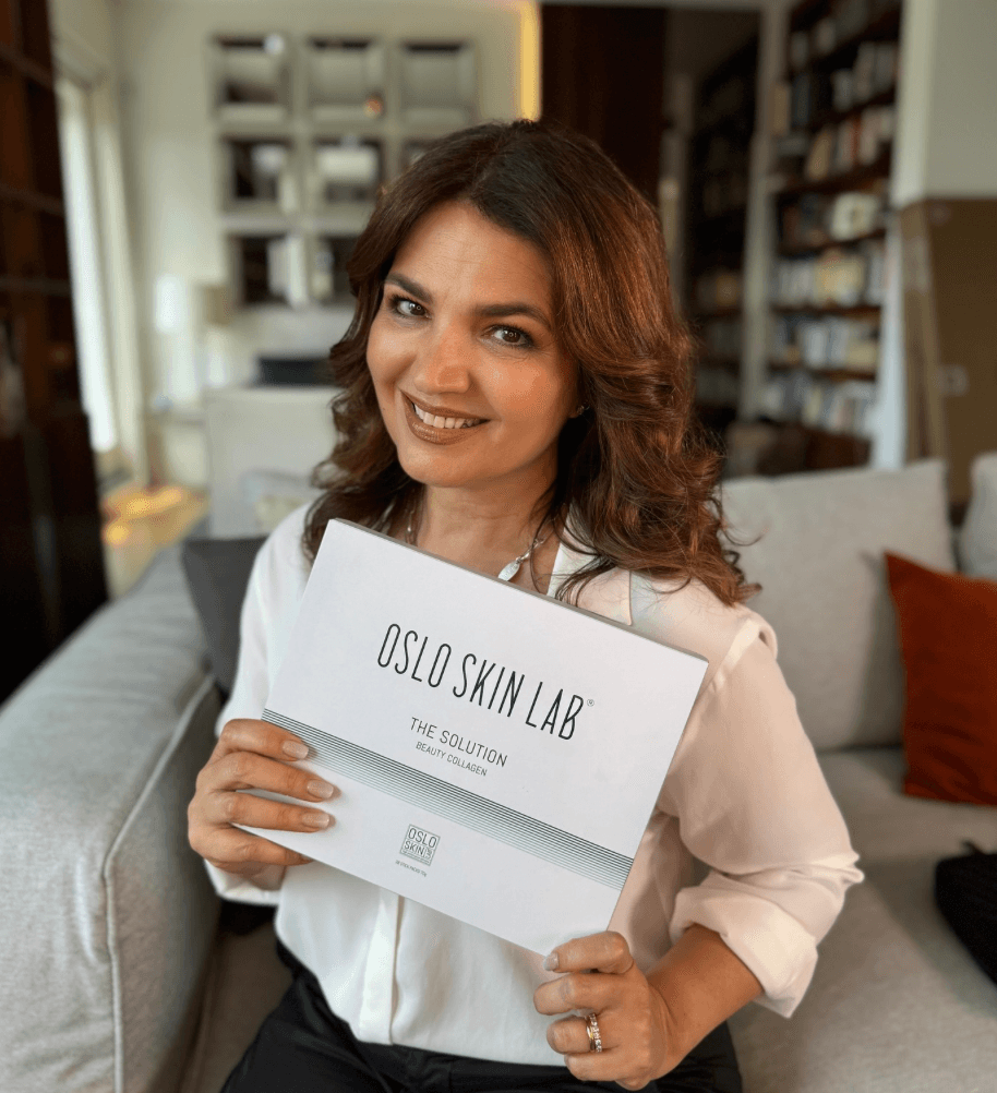 Donna sorridente con capelli castani che tiene una scatola di collagene Oslo Skin Lab.