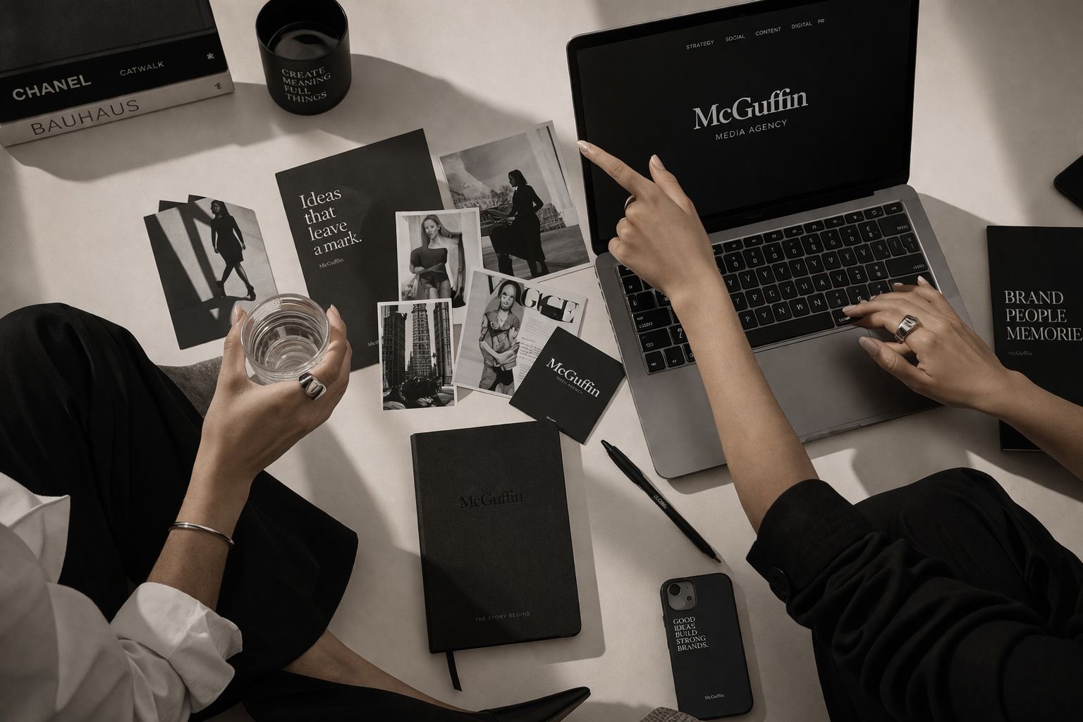 Due persone lavorano su un laptop tra foto, taccuini neri e oggetti di design minimalista.