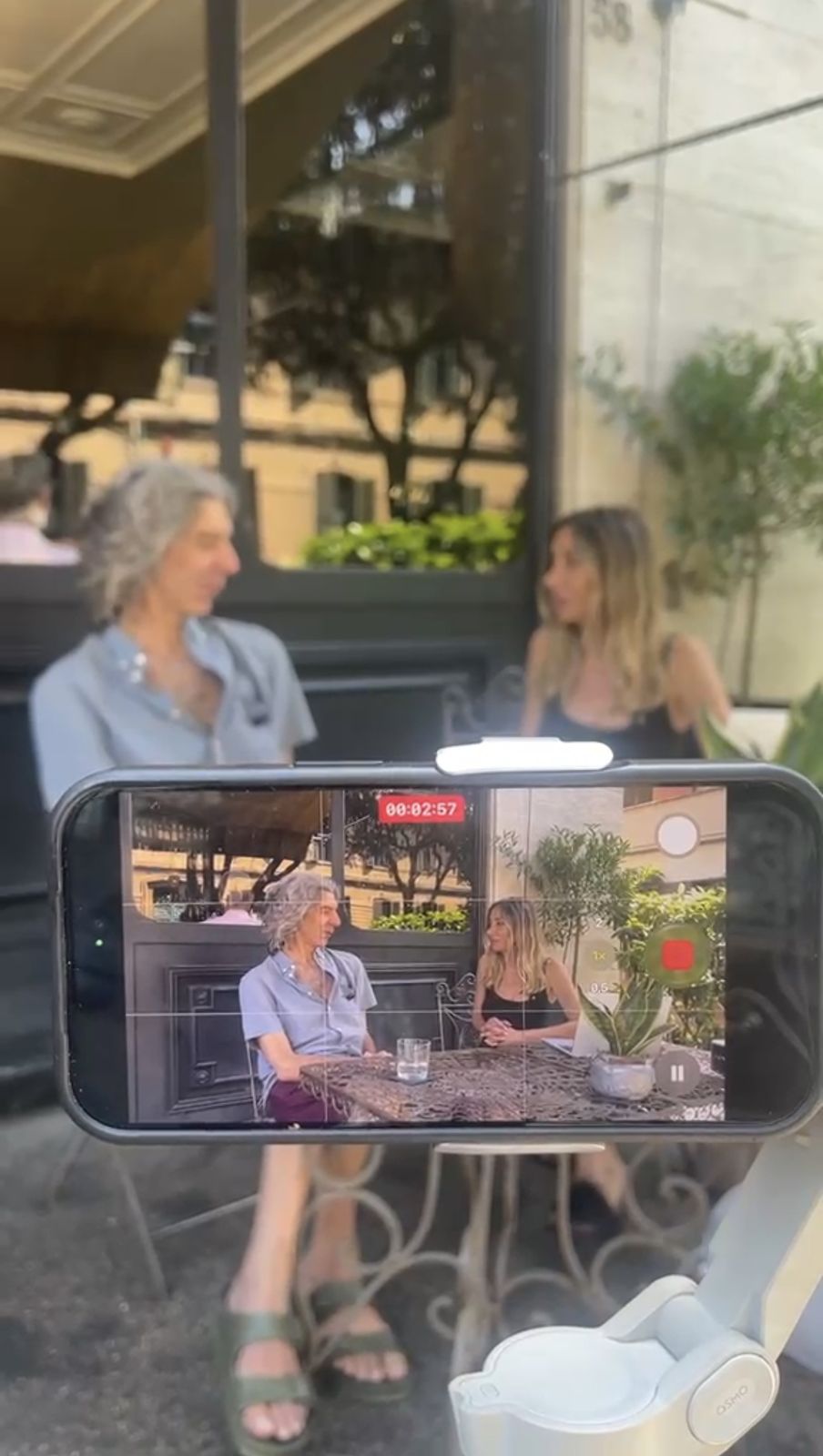 Smartphone su gimbal riprende un uomo e una donna seduti a un tavolo all'aperto.